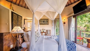 A bedroom with a canopy bed, a bedside table with a lamp, a chair, and a view of the outdoors.