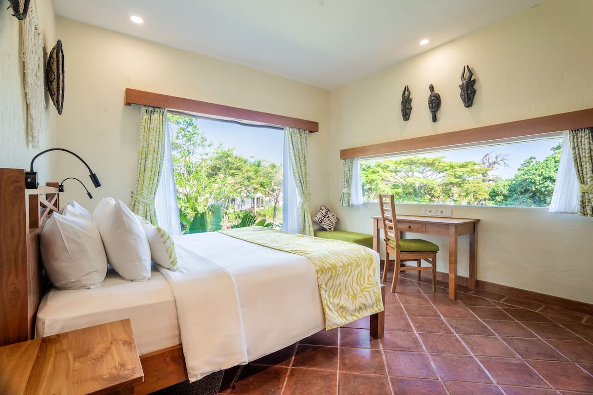 A bedroom with a bed, a desk, and a view of greenery.