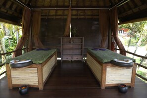 A wooden massage room with two massage tables, a shelf with a small plant, and a wooden bench. - Mara River Safari Lodge (Gianyar)