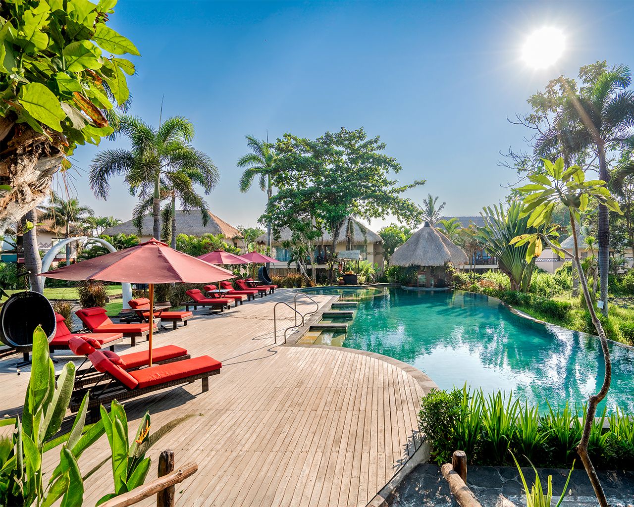 A poolside area with lounge chairs and umbrellas, surrounded by tropical vegetation.