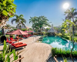 Área de piscina com espreguiçadeiras e guarda-sóis, cercada por vegetação tropical.