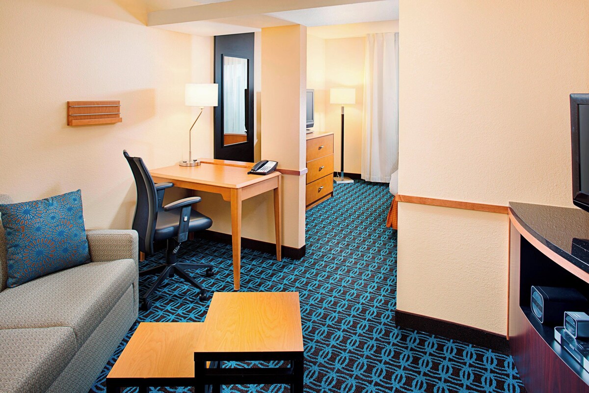 A hotel room with a sofa, a desk, a chair, a television, a lamp, and a dresser.
