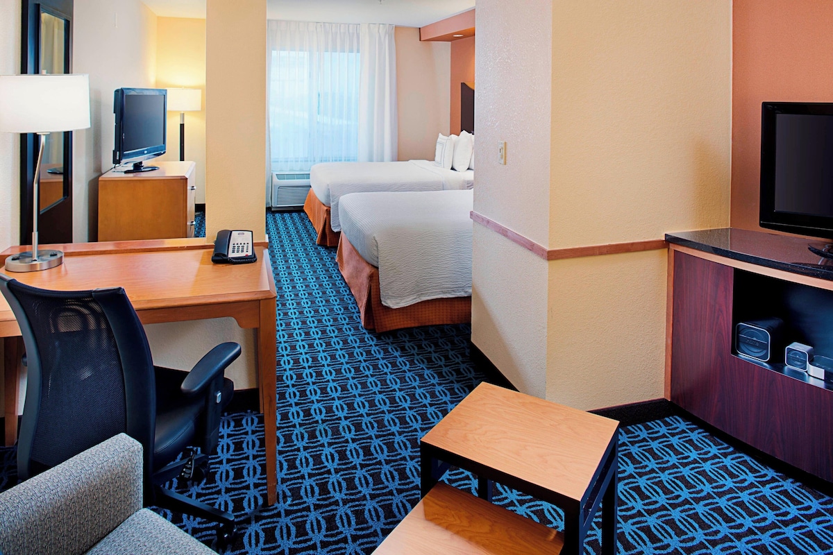 A hotel room with a desk, two beds, a TV, a phone, and a patterned carpet.