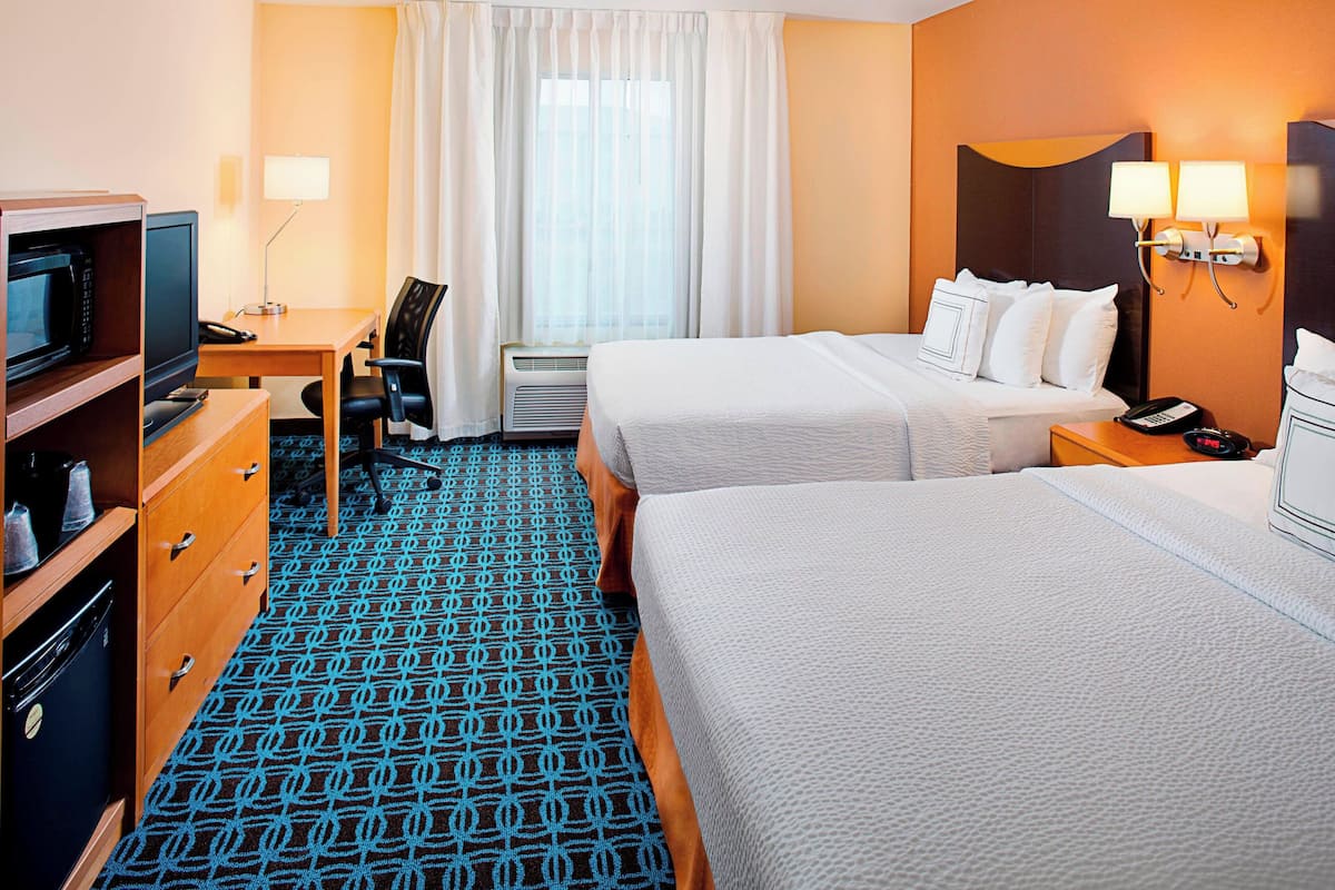 A hotel room with two beds, a desk with a computer, a TV, and a minibar.