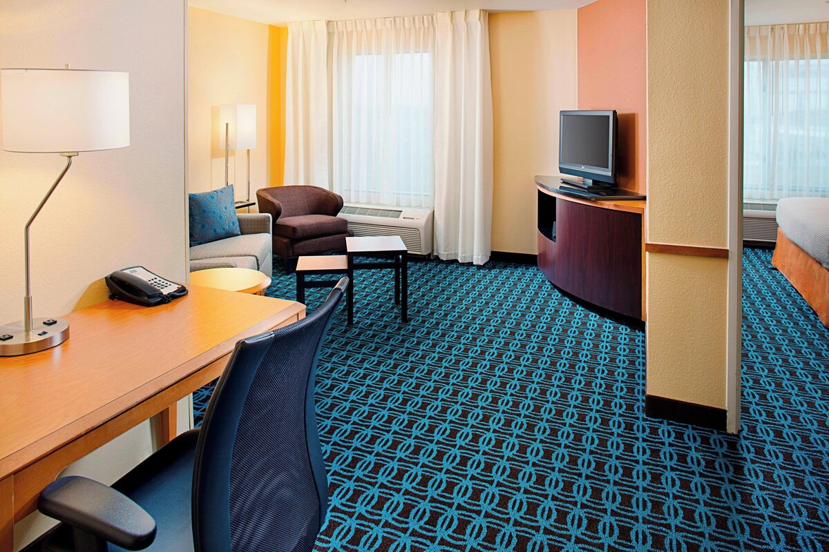 A hotel room with a desk, chair, television, and a patterned carpet.