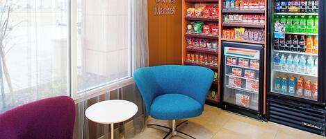 A corner market with a Pepsi refrigerator, snack shelves, and a blue chair near a window.