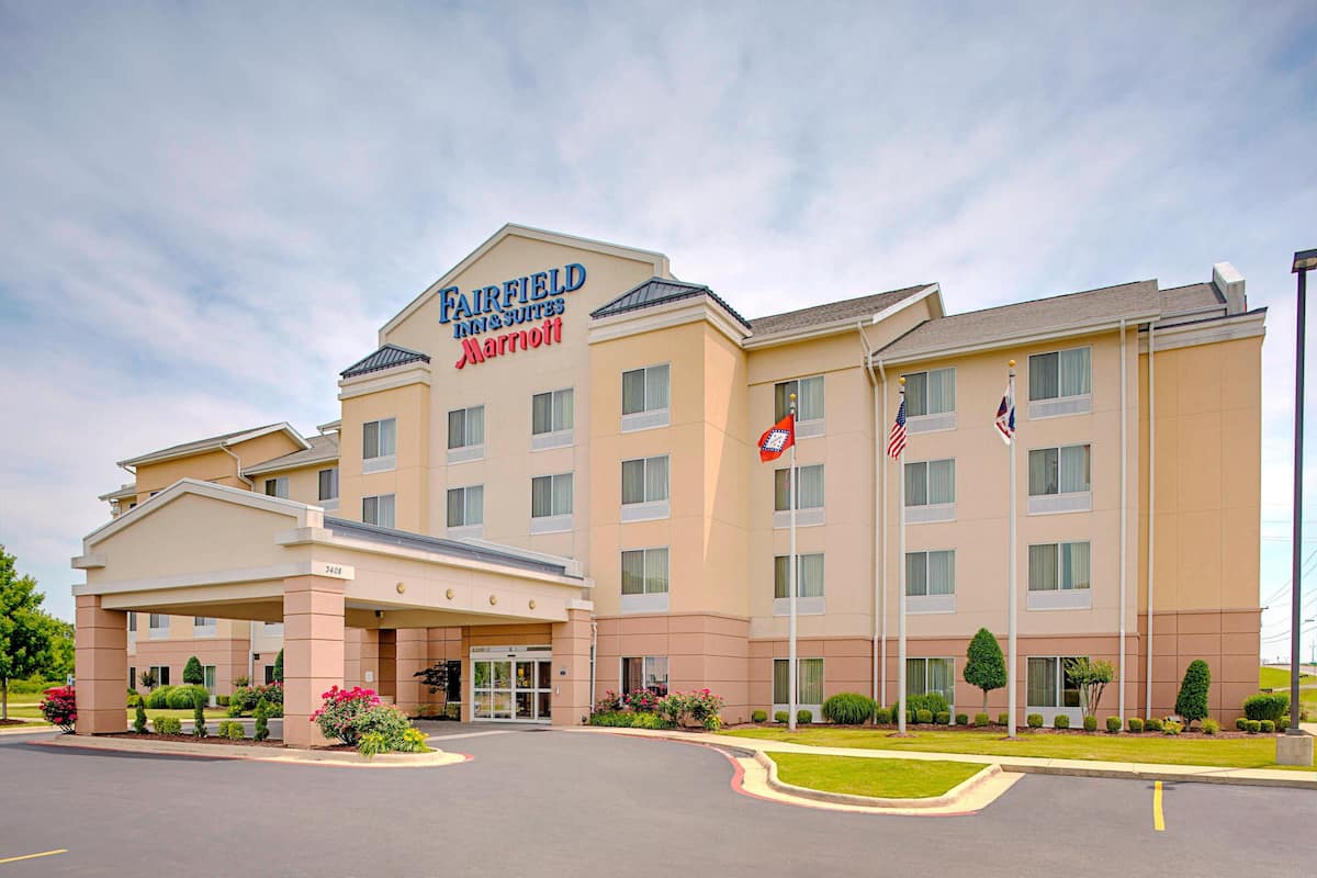 A Fairfield Inn & Suites by Marriott hotel with a covered entrance, multiple flags, and well-maintained landscaping.