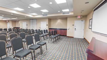 A conference room with rows of chairs, a podium, and a projector screen.