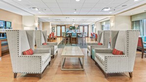 A spacious lobby with high-backed armchairs, a central coffee table, and a reception desk with computers. - Hampton Inn Denver Northeast-Brighton (Brighton)