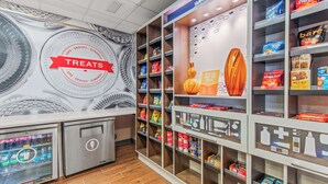 A snack and beverage kiosk with a 'TREATES' sign, shelves stocked with various snacks and beverages, and a 'Welcome to' sign above the entrance. - Hampton Inn Denver Northeast-Brighton (Brighton)