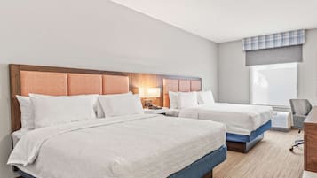 Habitación de hotel con dos camas, un escritorio, una silla y un ventanal amplio.