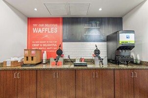 Una estación de gofres con un letrero rojo, dispensadores de masa para gofres y una máquina para gofres.