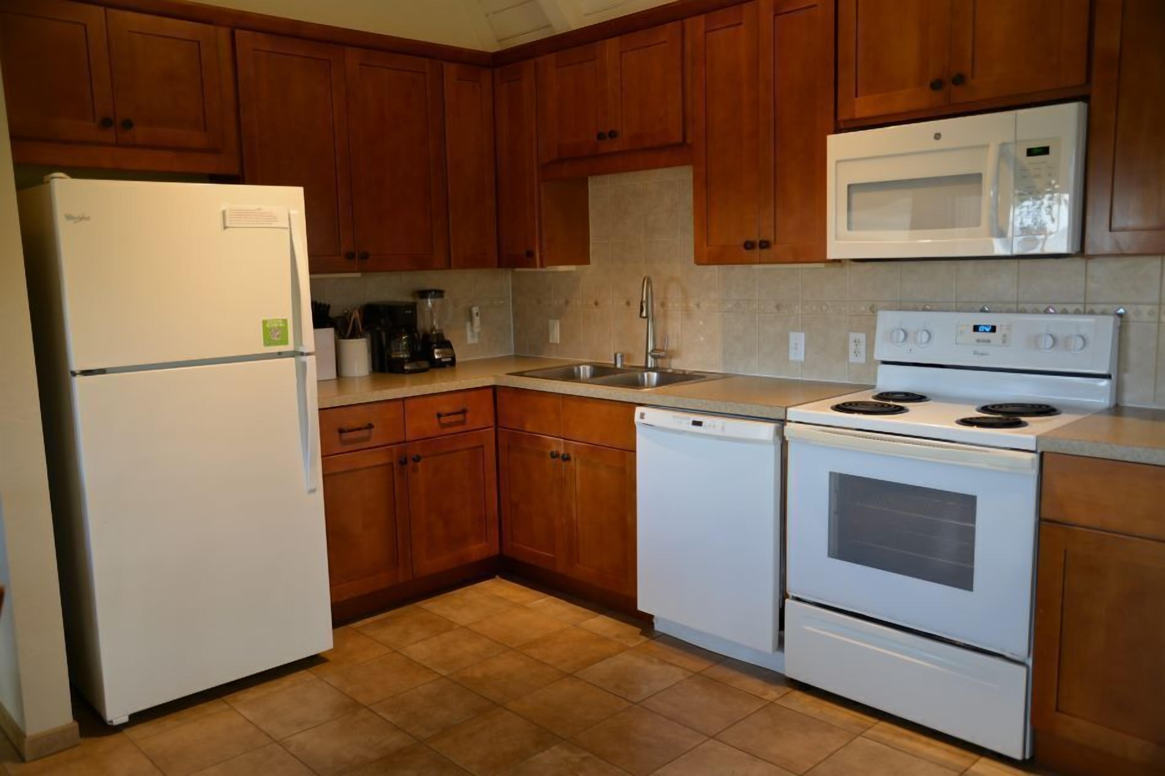 A kitchen with wooden cabinets, a white refrigerator, a microwave, a dishwasher, and a stove.