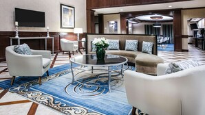 Un hall d’hôtel avec une table basse ronde, des canapés, des fauteuils, un téléviseur et une moquette à motifs.