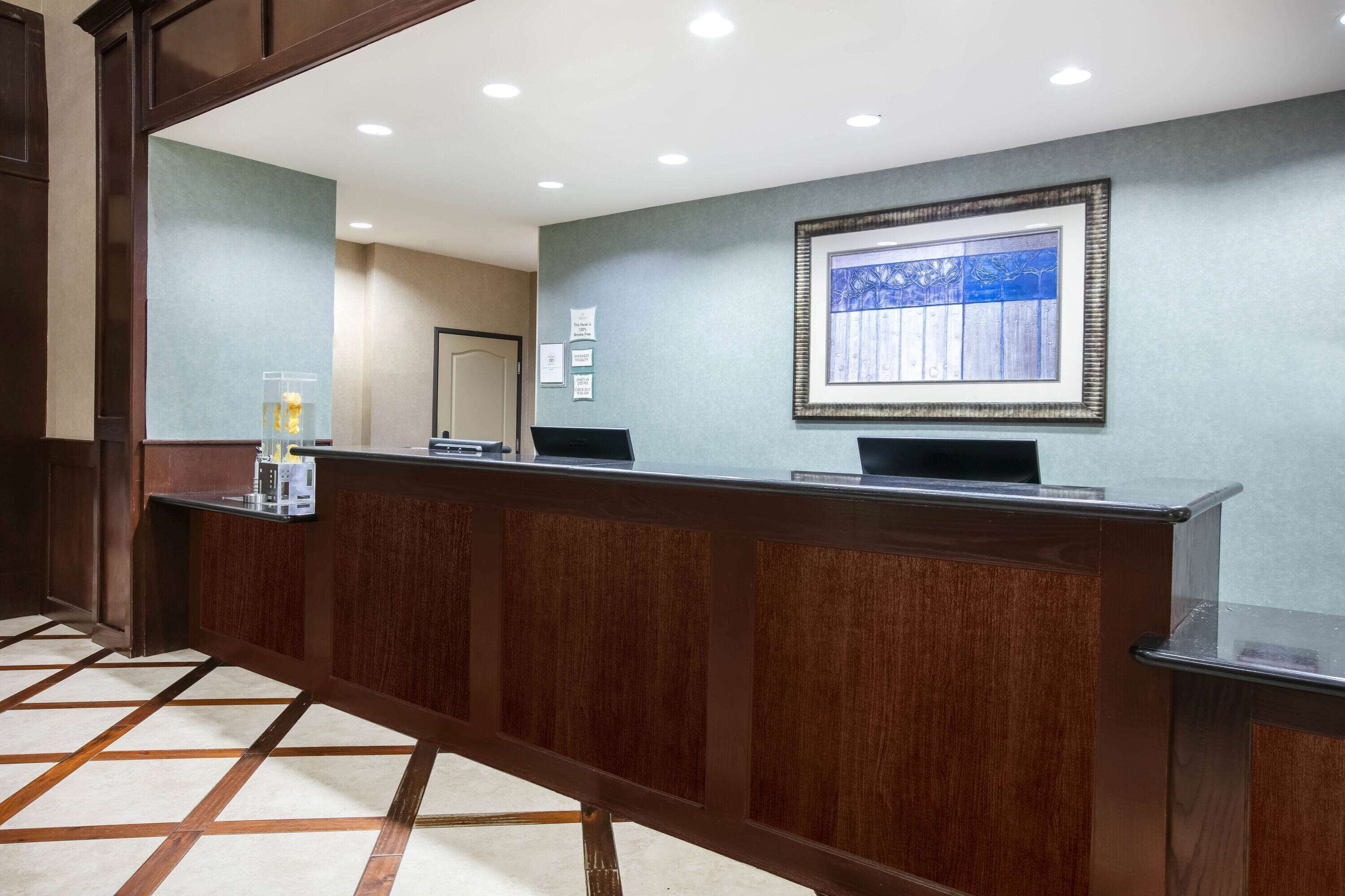 A reception area with a wooden reception desk, a framed artwork on the wall, and a tiled floor.
