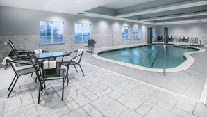 Une piscine intérieure avec un sol carrelé, une table de billard et plusieurs chaises.