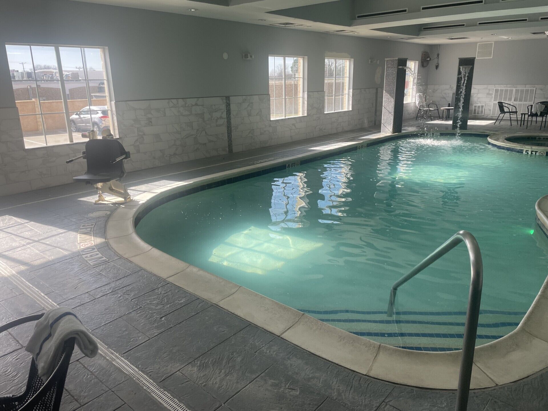 An indoor swimming pool with clear water, a diving board, and a chair.
