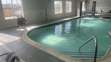 An indoor swimming pool with clear water, a diving board, and a chair.