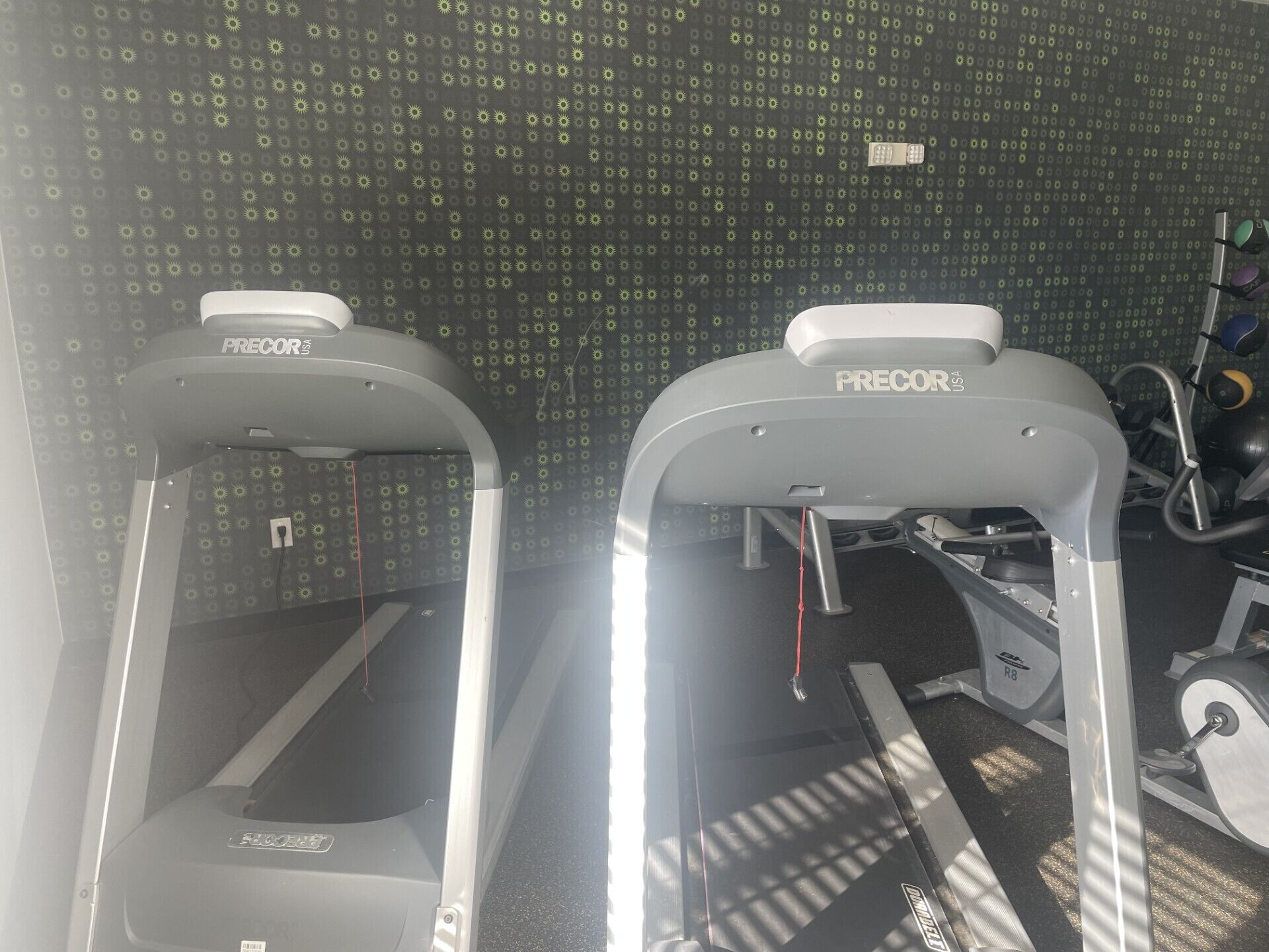 Two treadmills labeled 'PRECOR' in a gym with patterned walls and exercise equipment in the background.