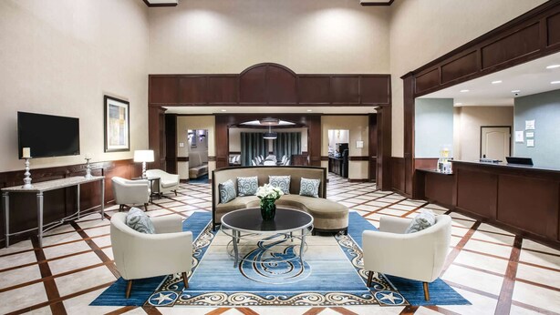 Un hall d’entrée spacieux, avec un grand canapé, deux fauteuils, une table basse et un téléviseur.