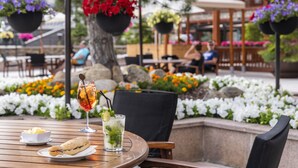 An outdoor dining area with a round wooden table, a glass of iced beverage with a straw, and a sandwich on a plate. - Sport Village (Soldeu)