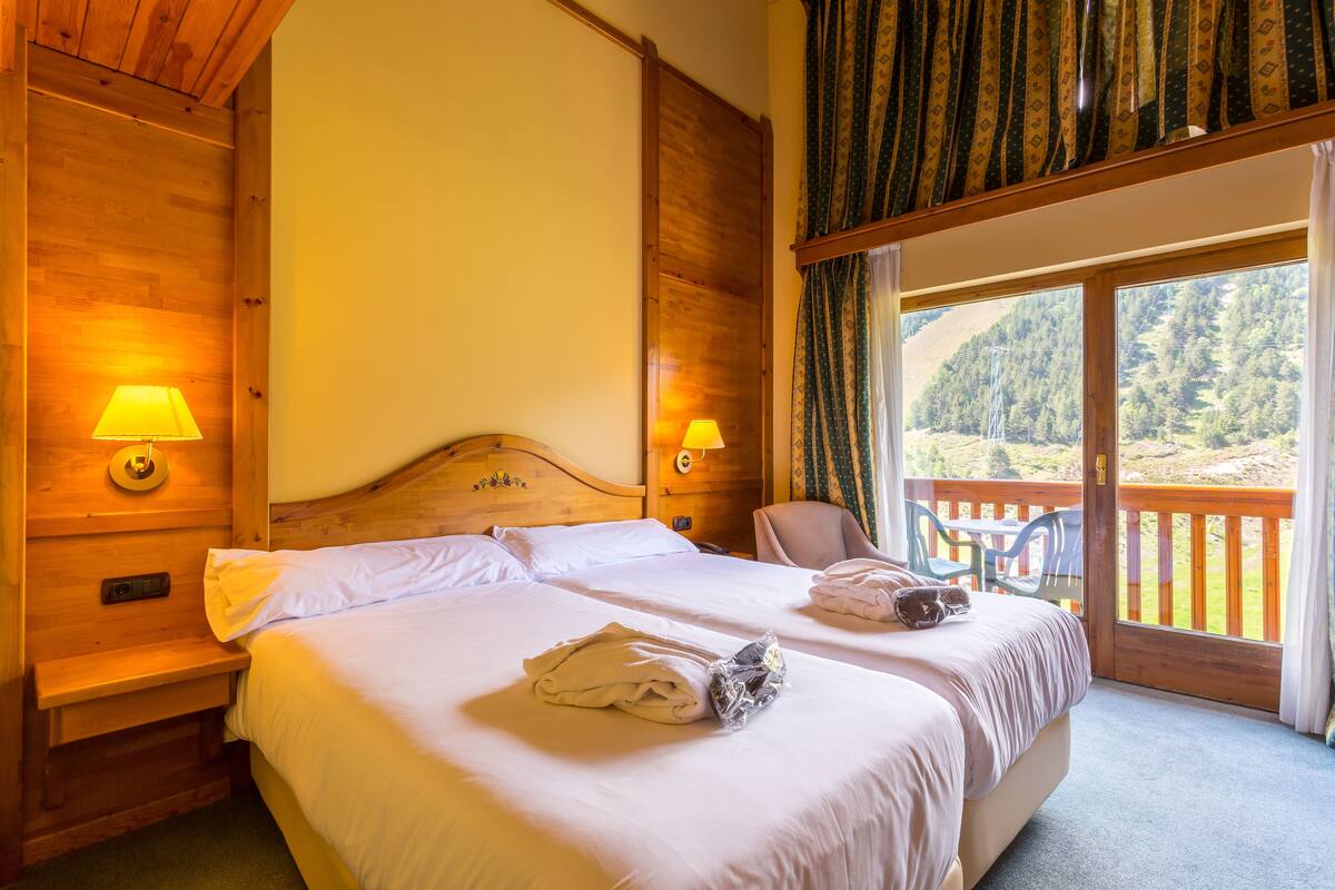 A double room with two beds, wooden headboards, and a balcony with a view of the forest.
