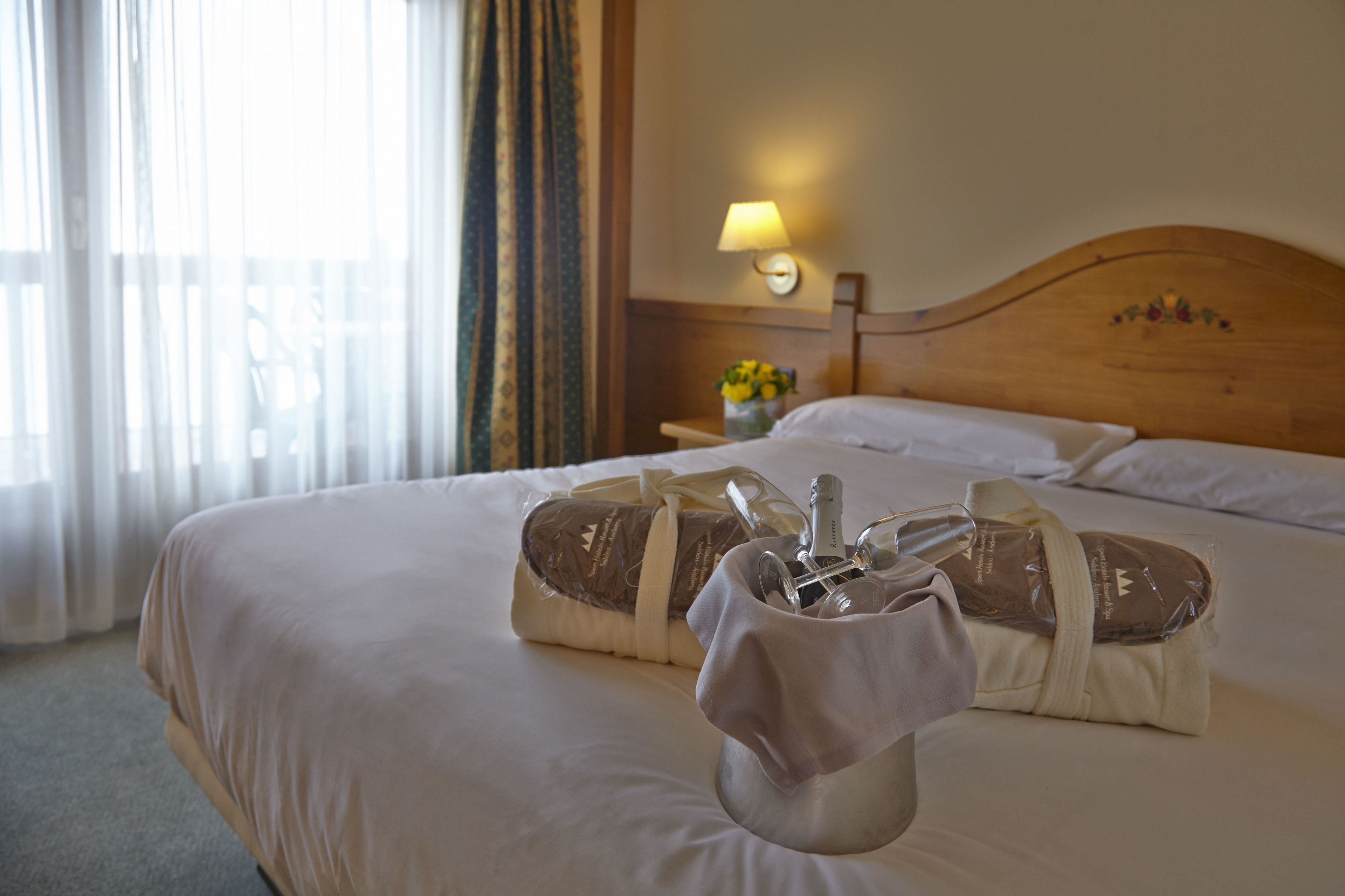 A hotel room with a neatly made bed, a bedside lamp, and a small table with a vase of flowers.