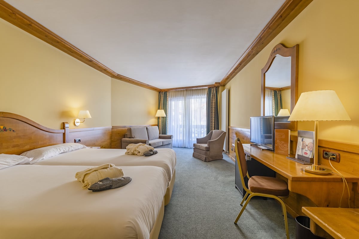 A hotel room with two beds, a desk, a chair, a TV, and a mirror.