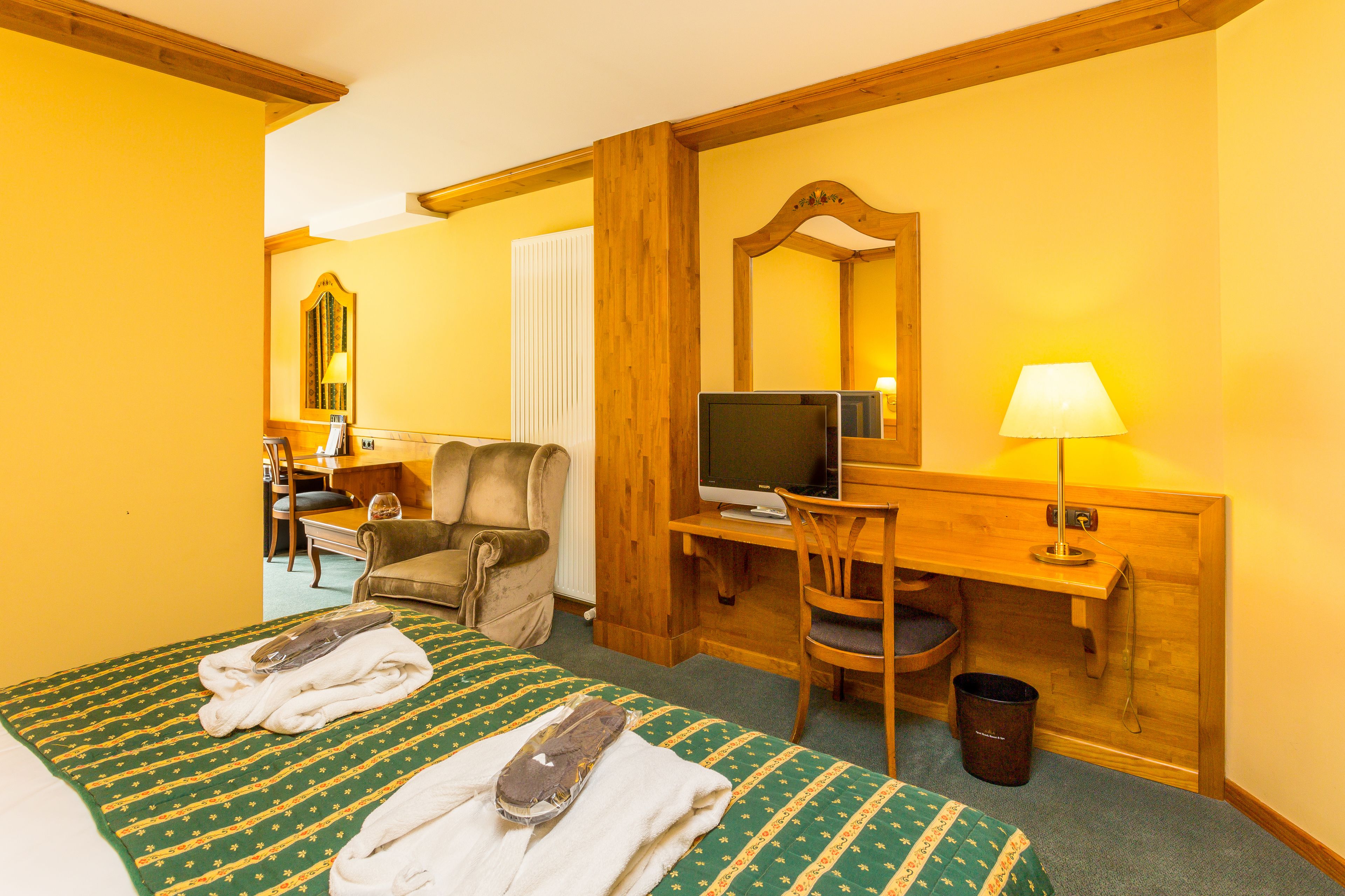 Habitación de hotel con cama, escritorio con computadora, silla, espejo y lámpara.