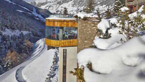 A mountain lodge with a glass elevator, snow-covered slopes, and a clear sky. - Sport Village (Soldeu)
