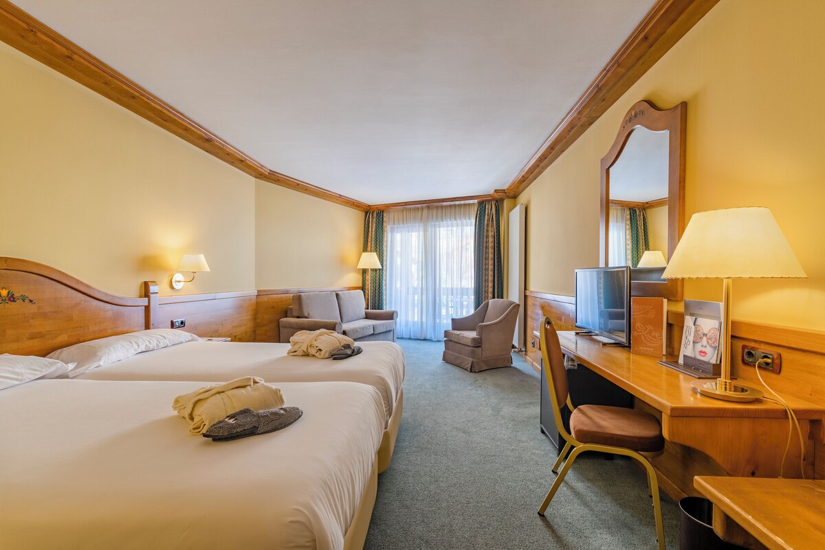 A hotel room with two beds, a desk, a chair, a TV, and a mirror.