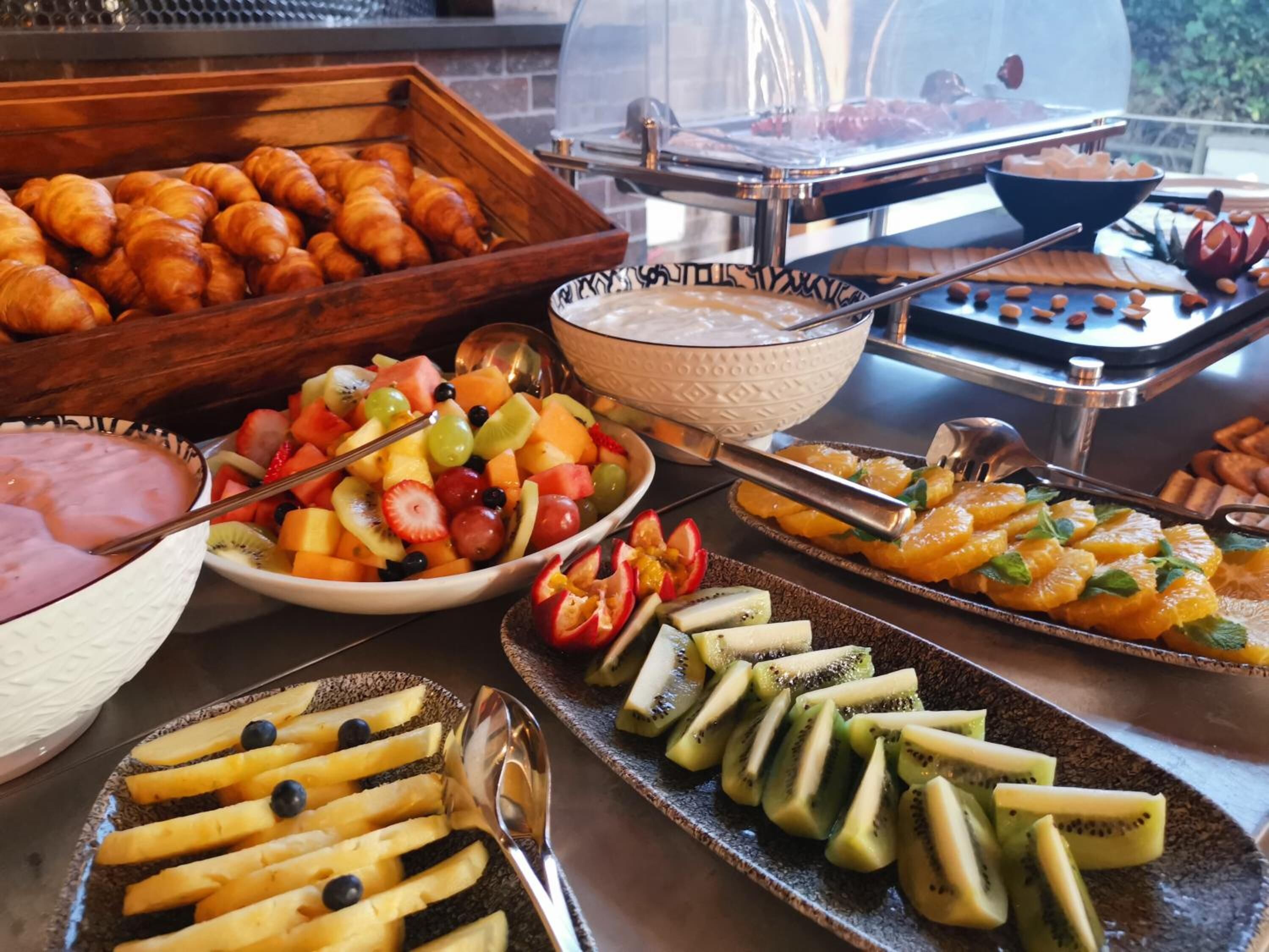 Buffet com diversas opções de comida, incluindo frutas, doces e uma área de grelhados.