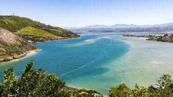 Un paisaje costero con una extensa masa de agua, colinas verdes y montañas a lo lejos.