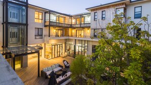 Un bâtiment moderne à plusieurs étages, doté d’une façade en verre, d’un espace extérieur aménagé pour s’asseoir et d’une terrasse en bois.