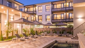 Une cour d’hôtel avec des espaces de détente en plein air, une piscine et un immeuble à plusieurs étages doté de balcons.