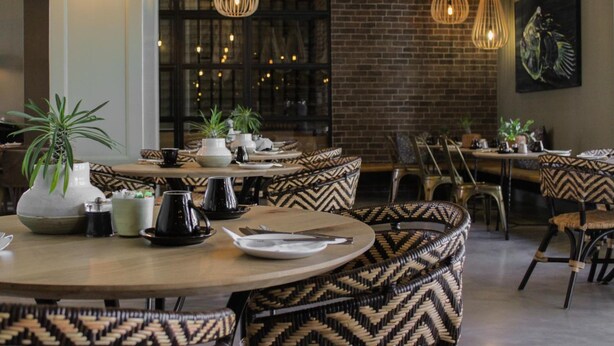 Un restaurant avec des tables rondes, des chaises à motifs, des luminaires suspendus et des plantes en pot.