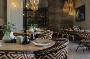 A restaurant with round tables, patterned chairs, hanging light fixtures, and potted plants. - aha The Rex Hotel (Knysna)