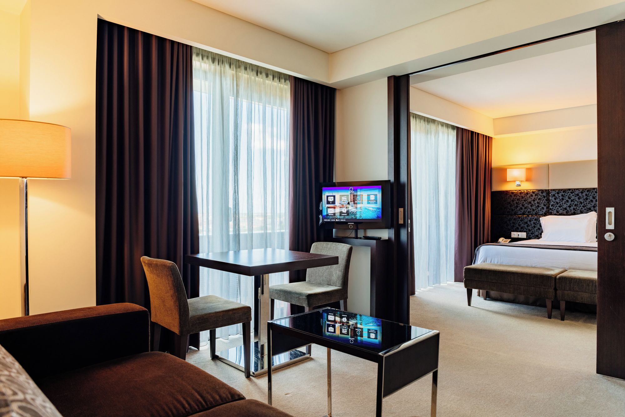 A hotel room with a bed, a desk with a chair, a television, and a sofa.