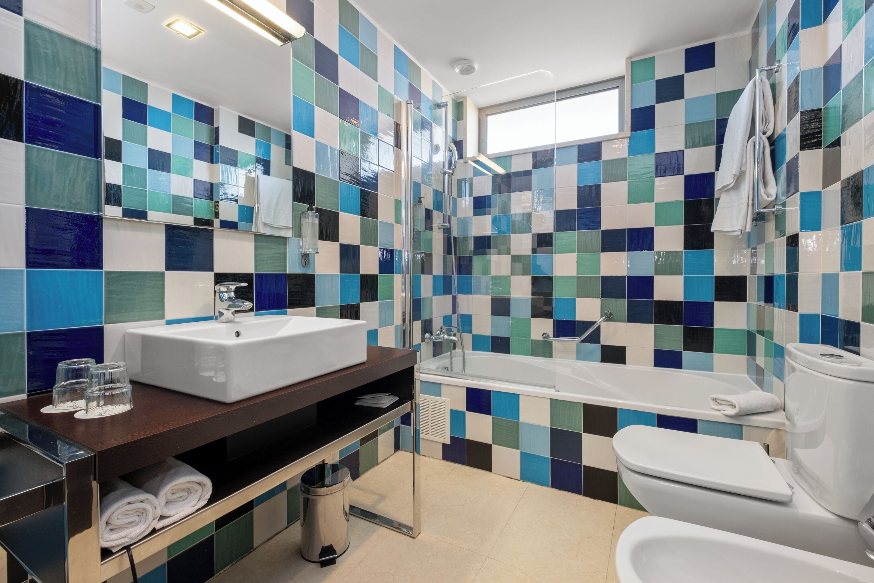 Un baño moderno con salpicadero de azulejos a cuadros, un lavabo blanco, una bañera y un inodoro.