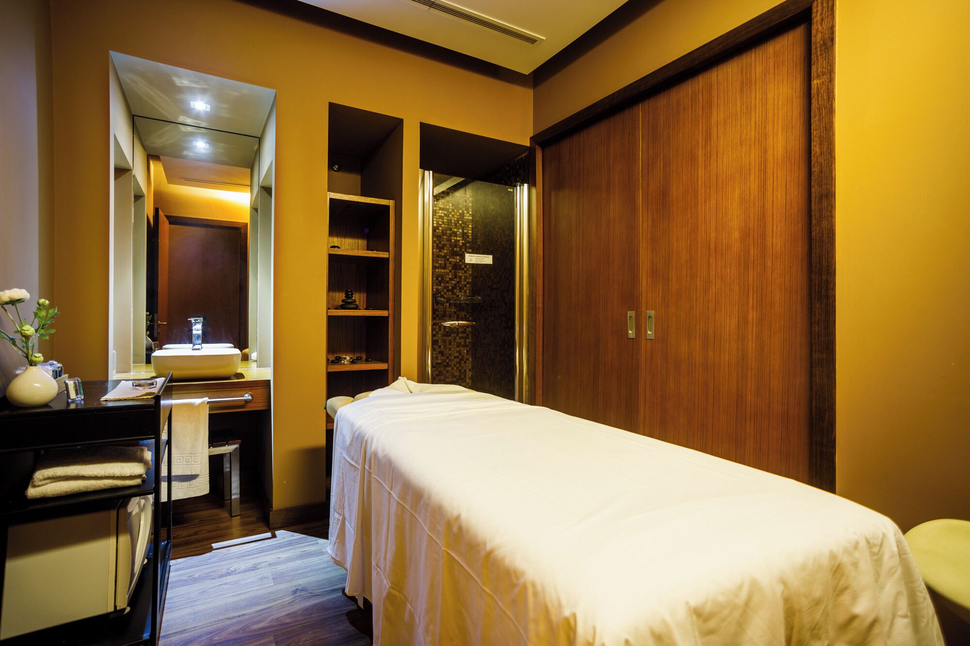 Una habitación de hotel con cama, tocador con espejo, lavamanos y armario de madera.