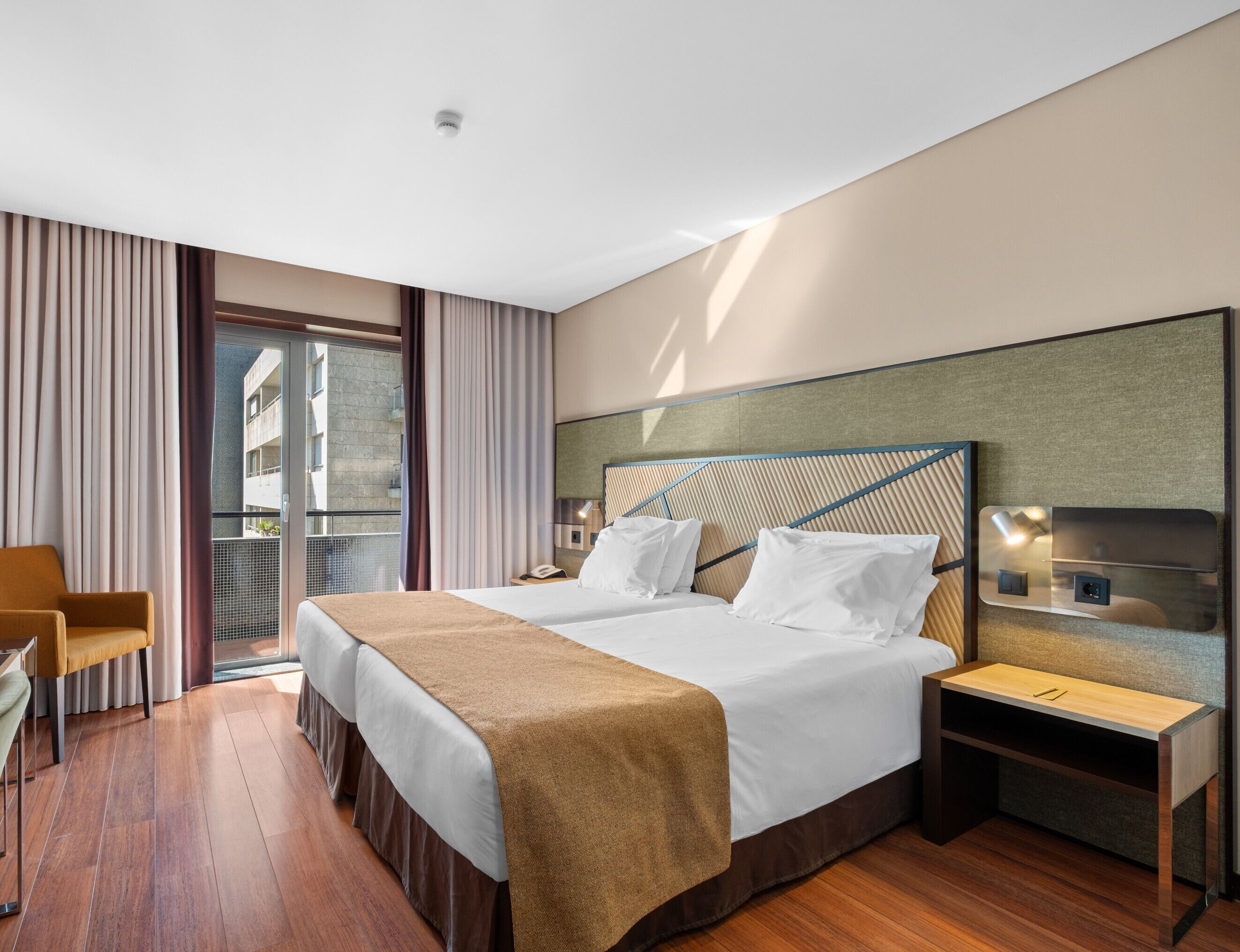 A hotel room with a bed, bedside tables, a chair, and a view of the outside.