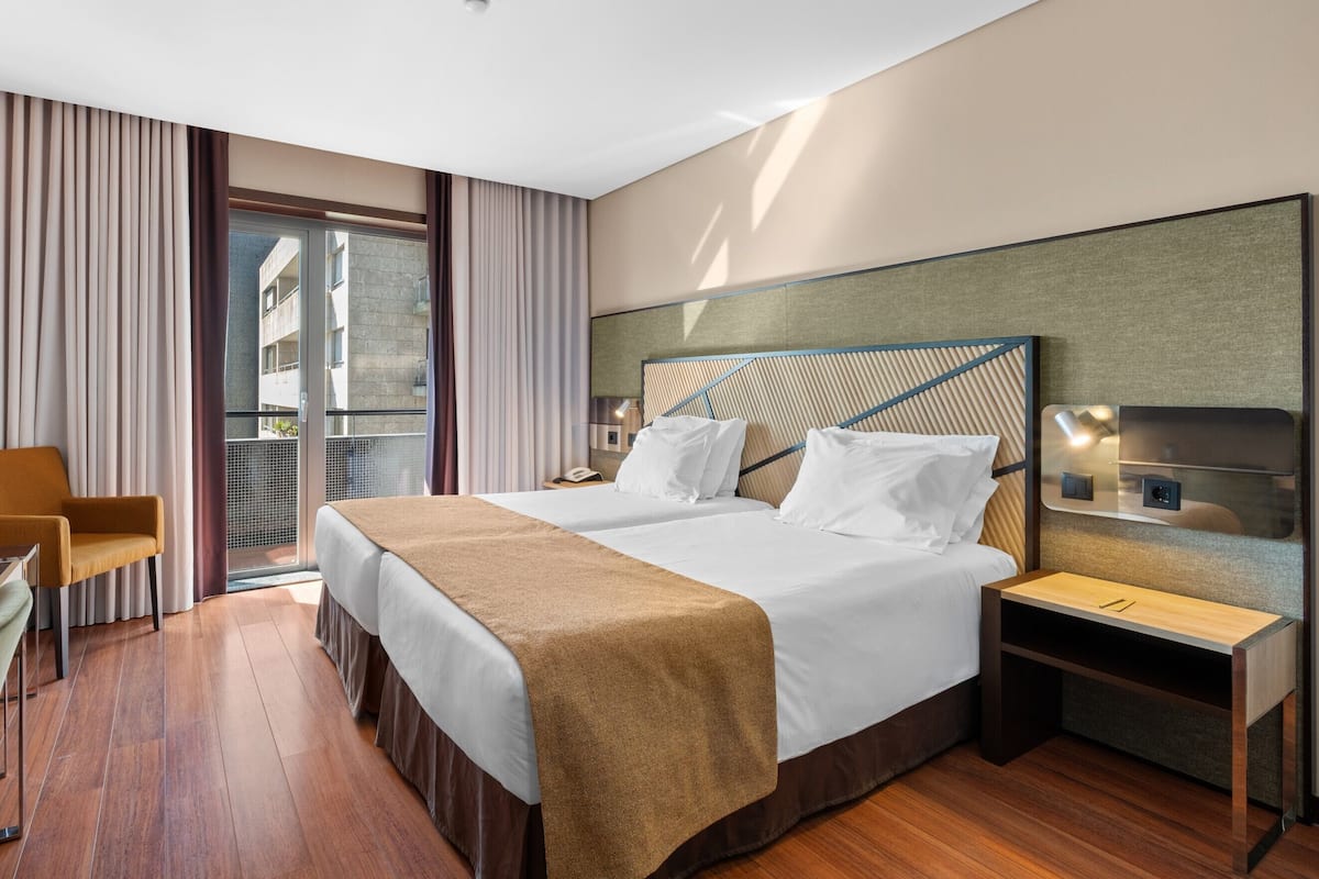 A hotel room with a bed, bedside tables, a chair, and a view of the outside.