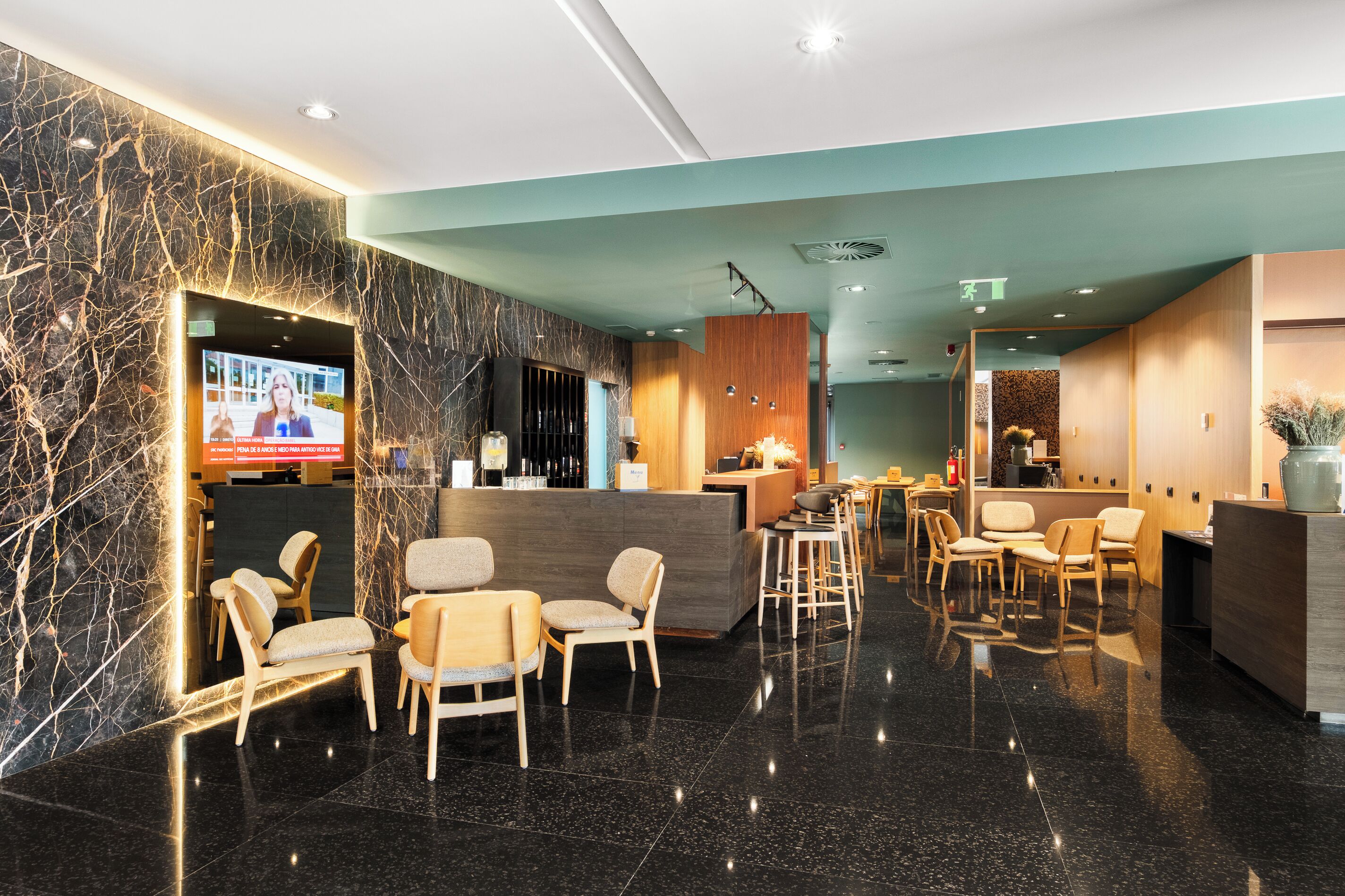 Un moderno vestíbulo de hotel con mostrador de recepción de mármol, zona de estar y una pantalla de televisión.