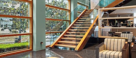 Un vestíbulo amplio con una escalera, zona de estar y grandes ventanales.
