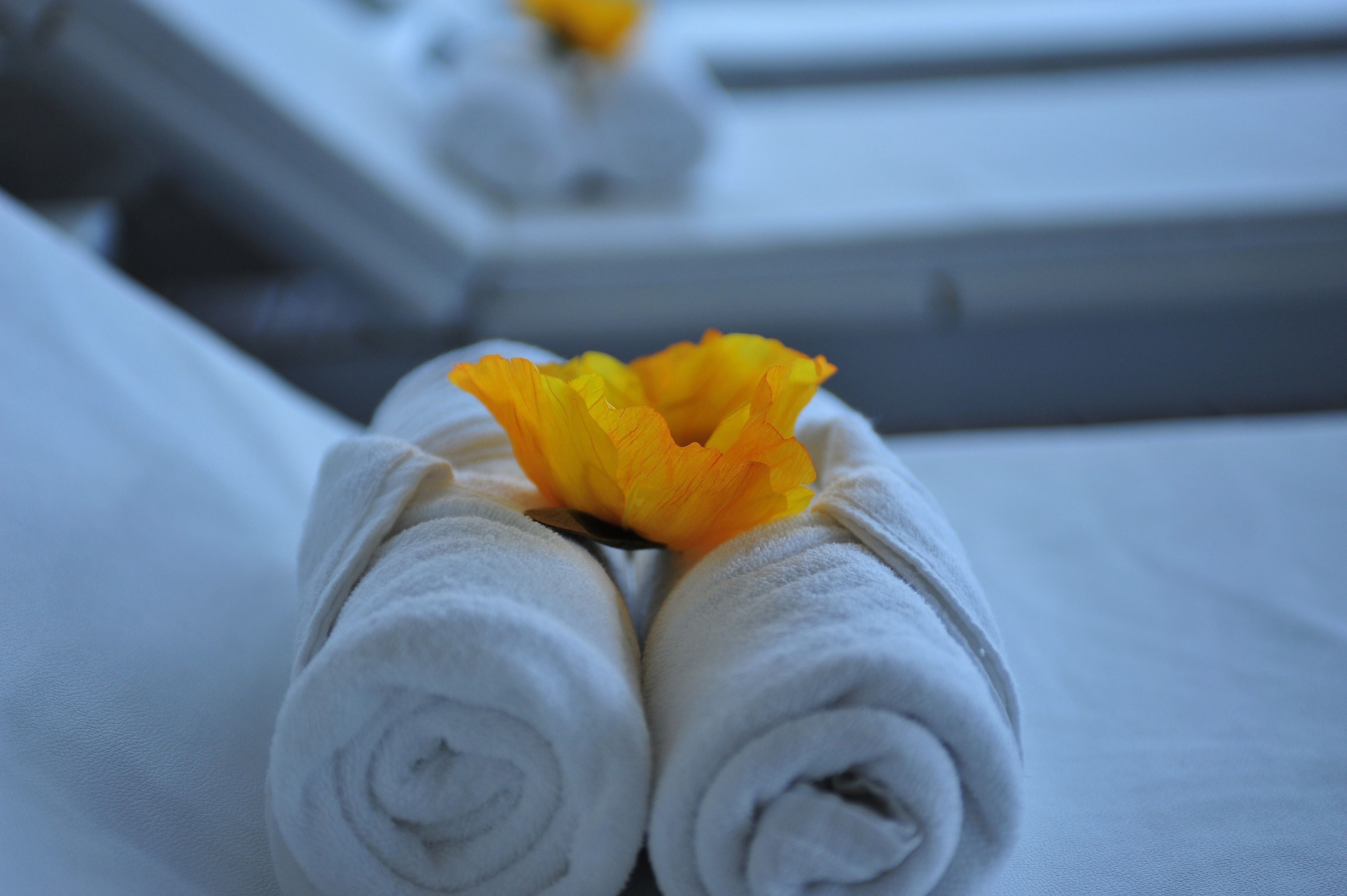 Toallas blancas enrolladas cuidadosamente con una flor amarilla encima, dispuestas sobre una cama.