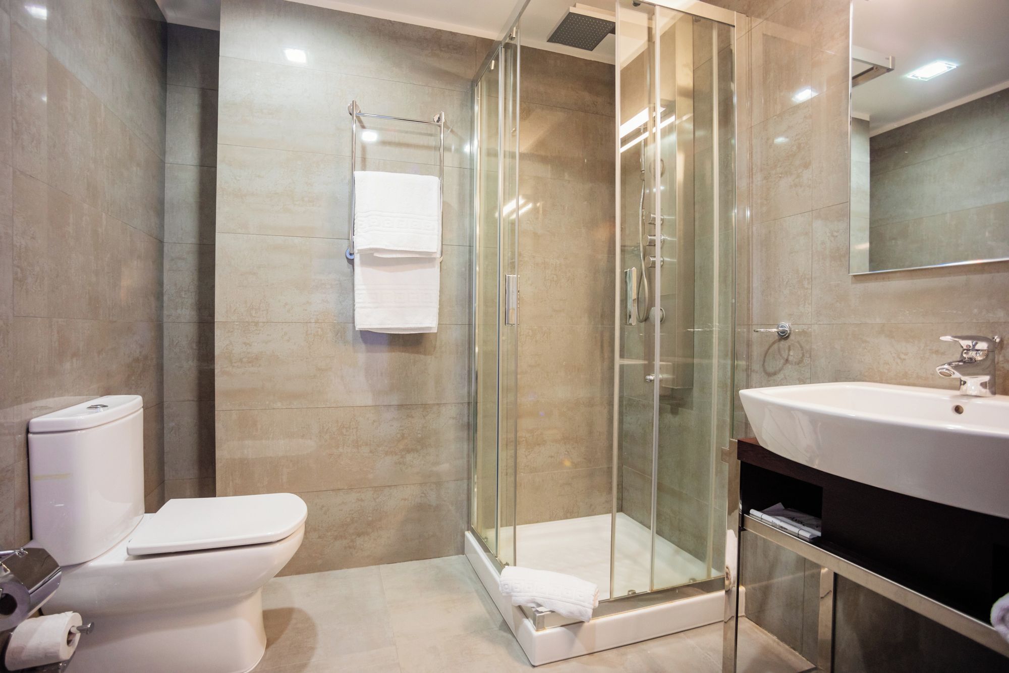 A modern bathroom with a glass-enclosed shower, a white toilet, and a sink with a mirror above it.