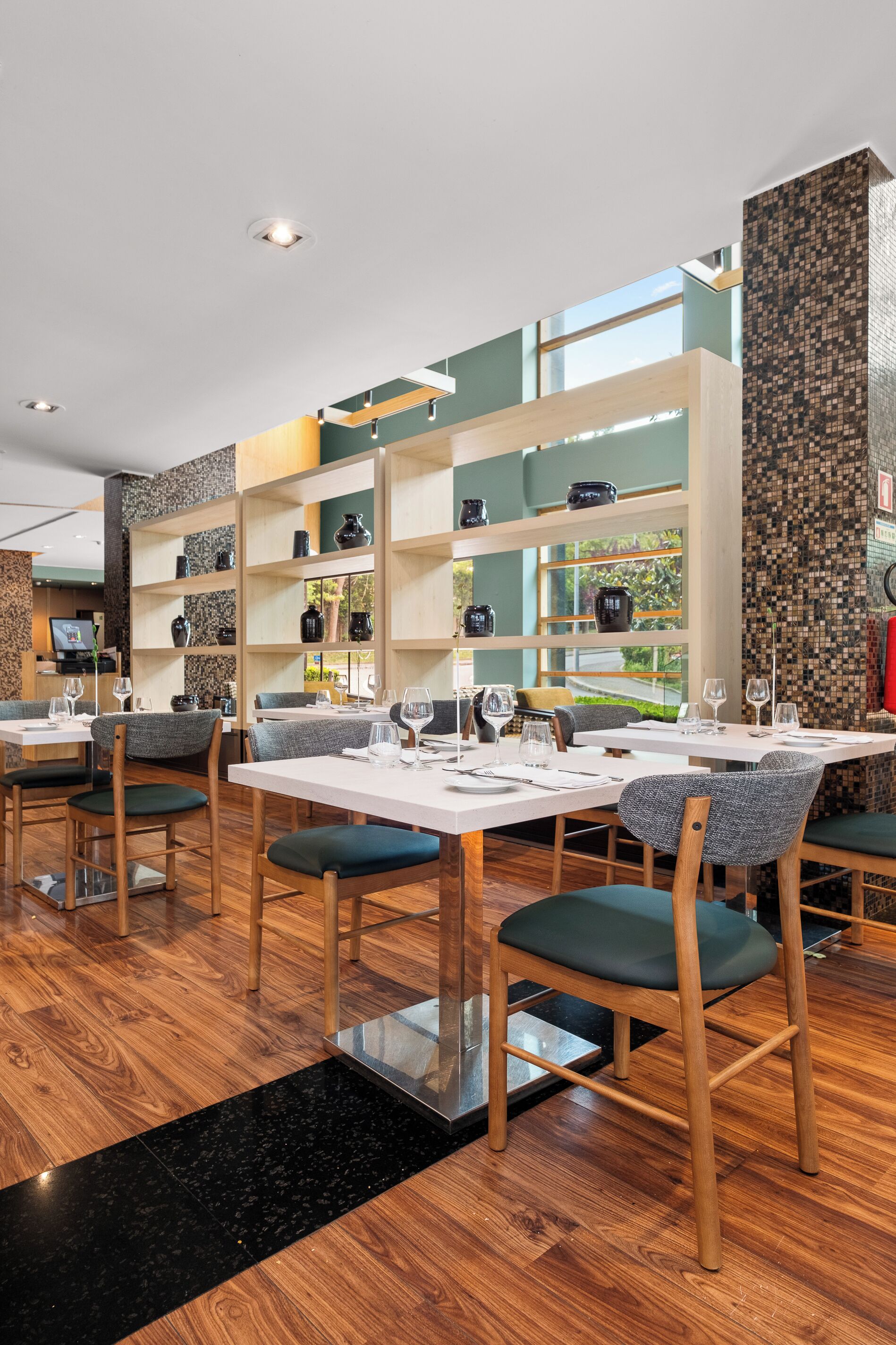 A restaurant interior with wooden flooring, tables with chairs, and shelves with decorative items.