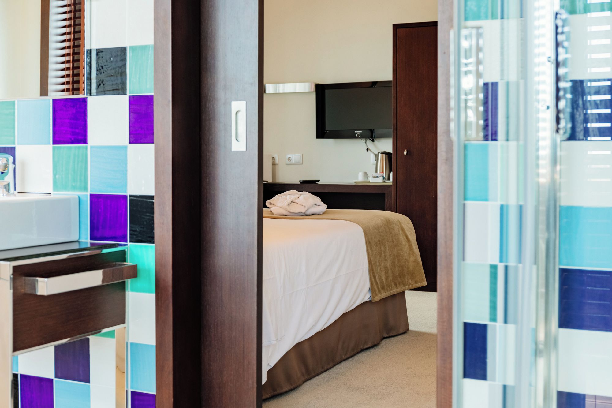 Habitación de hotel con cama, televisor y baño con espejo y lavamanos.