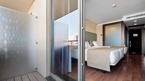 A modern hotel room with a large sliding door leading to a balcony, a bed with a beige cover, and a small table with a lamp. - Axis Porto Business & Spa Hotel (Matosinhos)