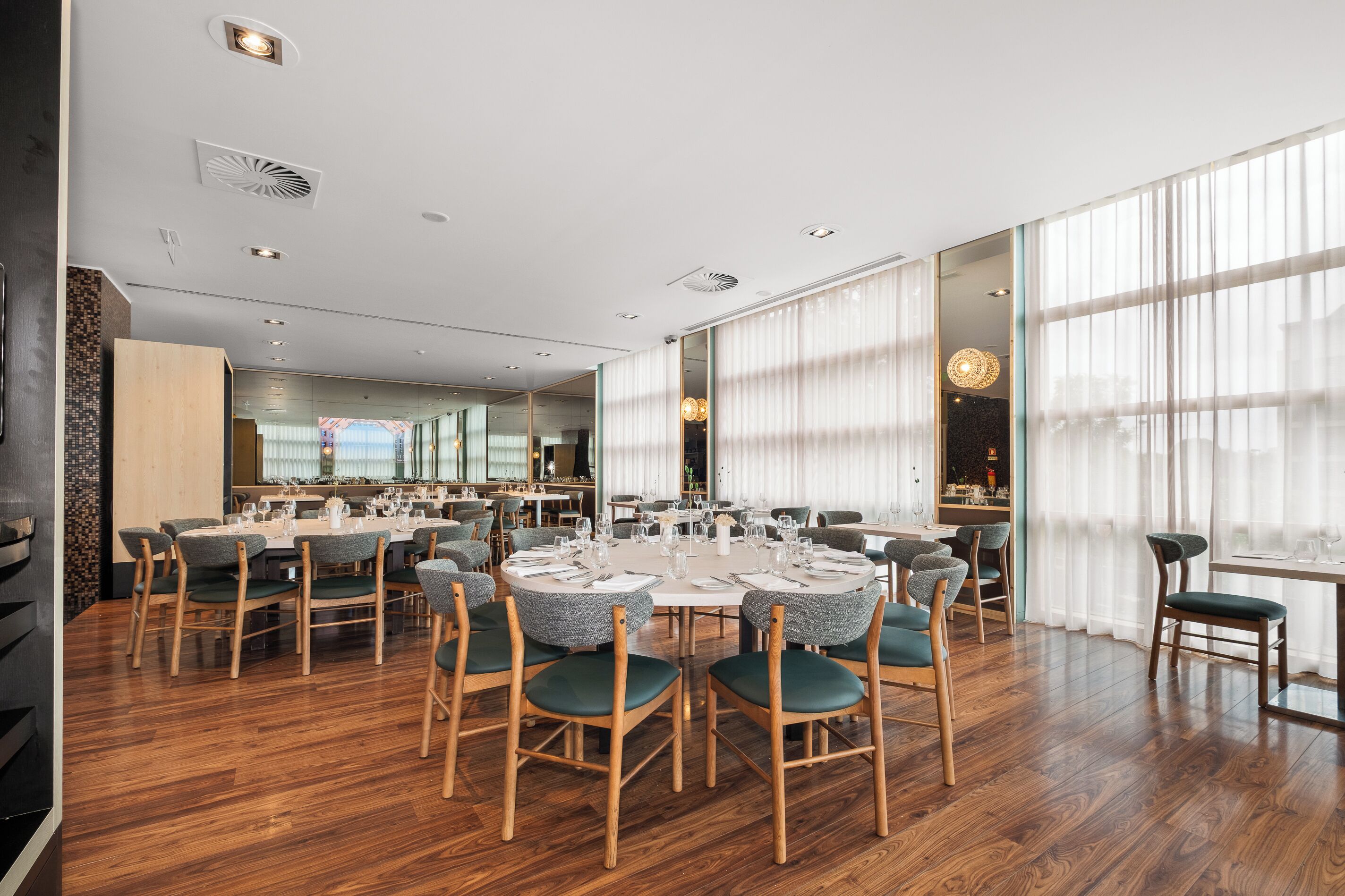 Un vaste espace dédié à la salle à manger, avec des tables rondes, des chaises et une vue sur la ville grâce à de grandes fenêtres.